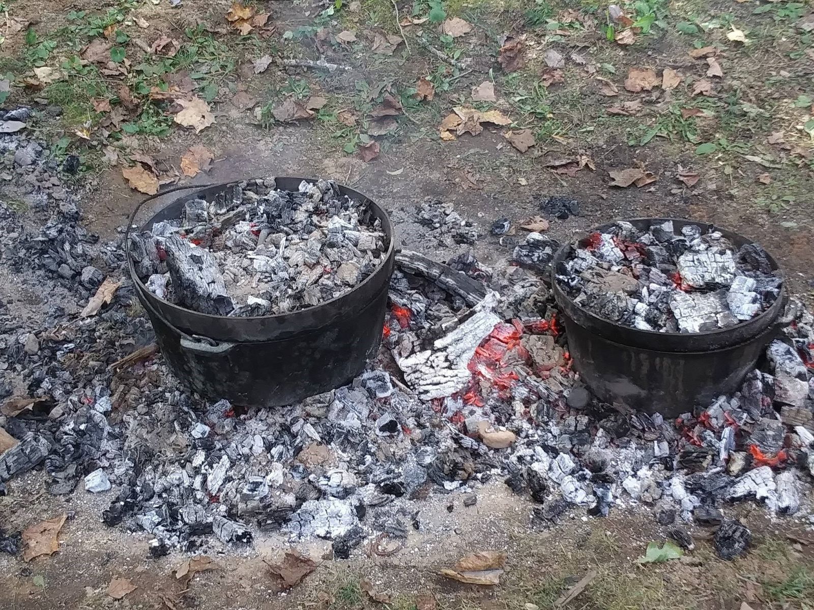 This image shows two different size cast iron dutch ovens being used while out camping above some hot coals