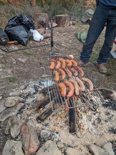 Sausages cooking on Auspit portable spit over open campfire