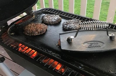 An image showing a charcoal bbq and burger patties being pressed down using a cast iron burger grill press 