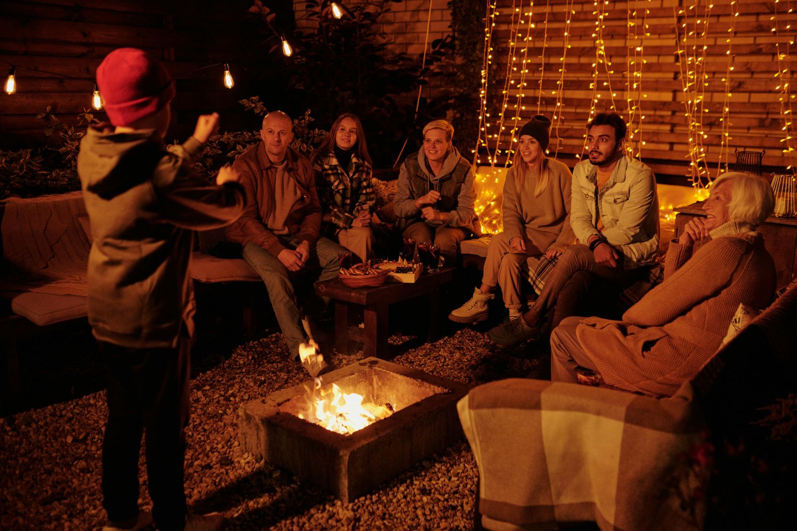 Group playing charades around a campfire with string lights at an outdoor campsite