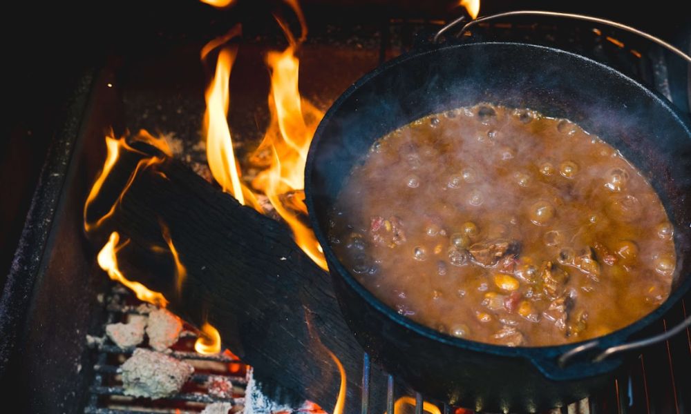 Cast iron pot with beef stew simmering over open fire flames