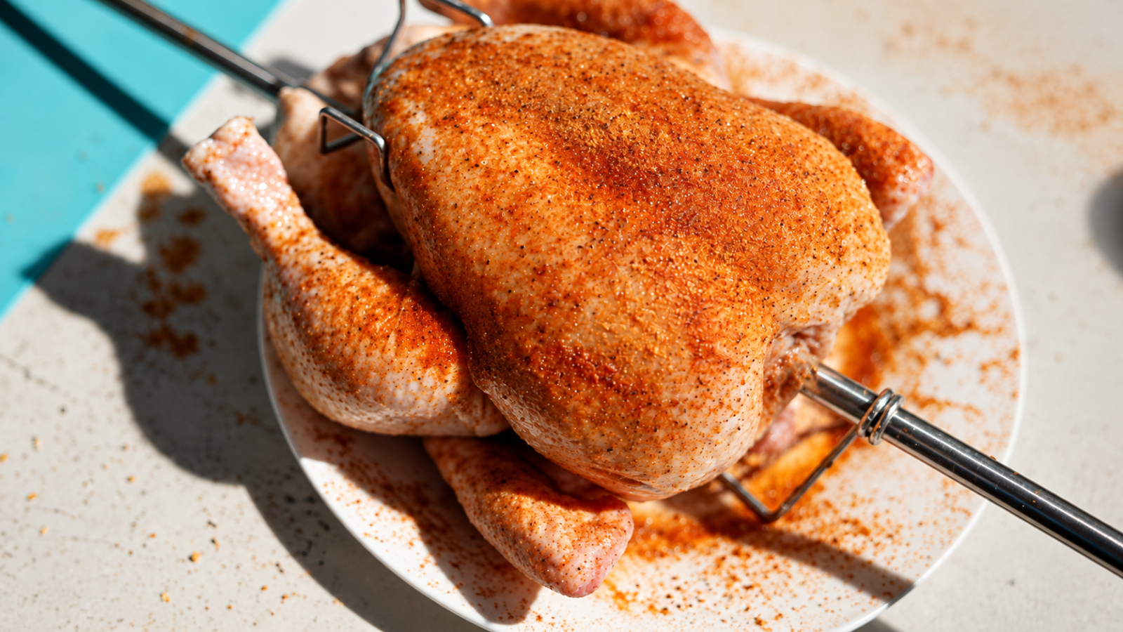 This image shows the whole chicken secured by chicken prongs on the skewer.