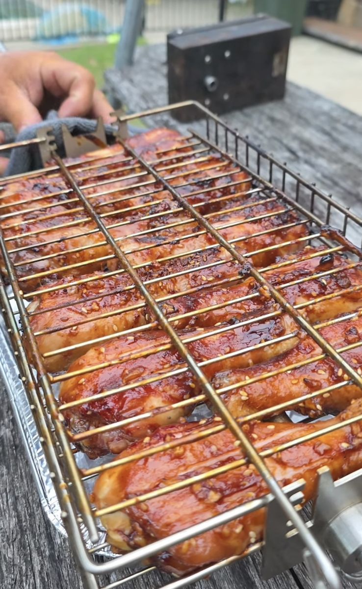 This image shows chicken wings being cooked on Auspit multi use basket on the Auspit portable camping spit.