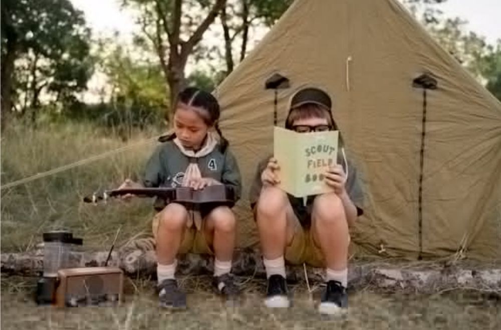 Two children sit in front of a canvas tent at a campsite—one playing a ukulele, the other reading a “Scout Field Book.” Camping gear and trees surround them in a grassy outdoor setting. Photo by Ron Lach : https://www.pexels.com/photo/kids-hanging-out-in-backyard-10045743/
