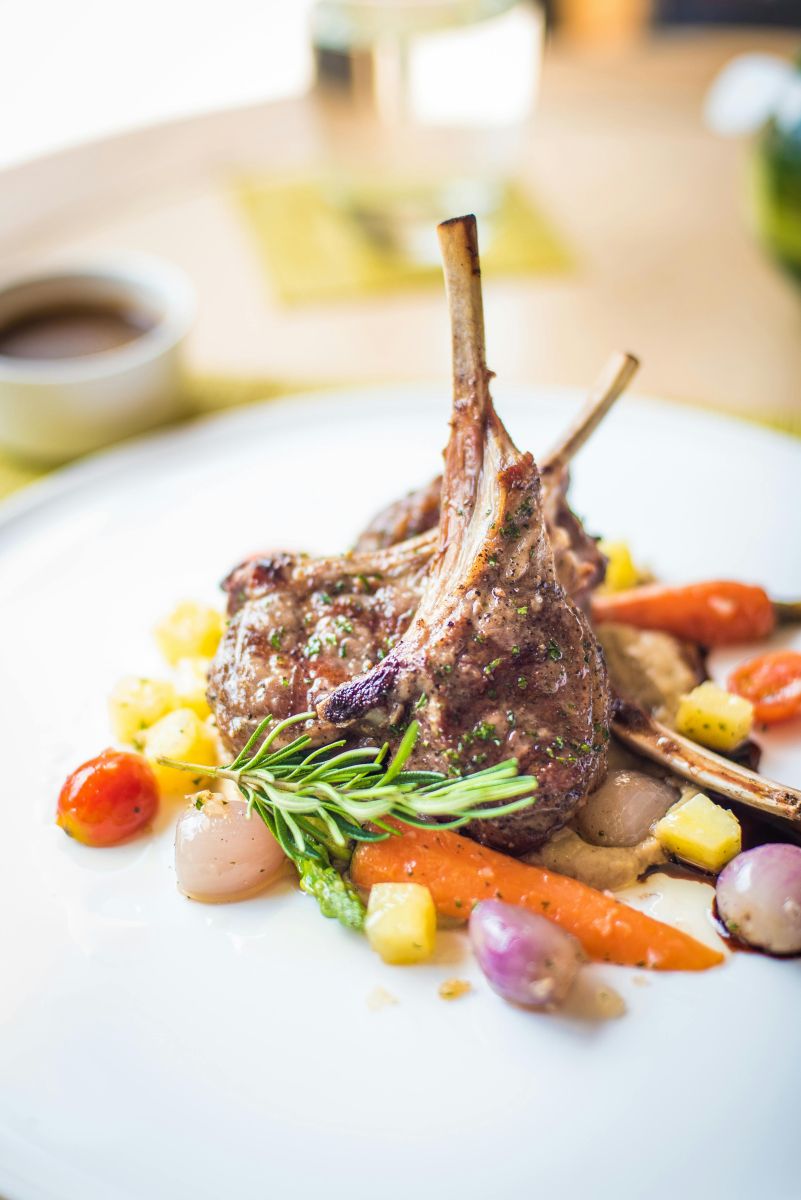 Plated lamb cutlets served with roasted vegetables and rosemary garnish.