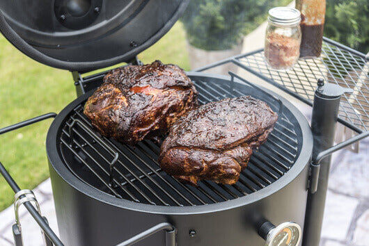 Juicy smoked pork cooking low and slow on a drum smoker with open lid, showing even heat and authentic charcoal flavour.