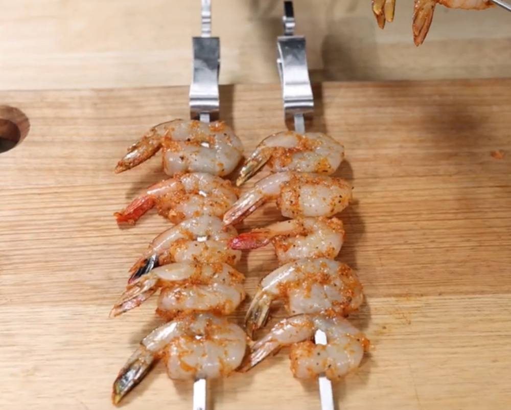Seasoned raw prawns threaded onto metal skewers on a wooden board