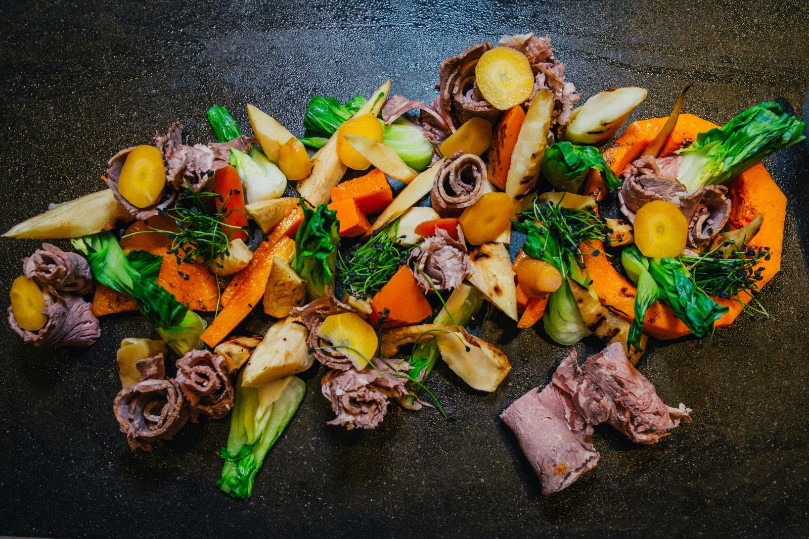 Slow cooked beef with roasted root vegetables, cabbage and gravy on a dark serving board