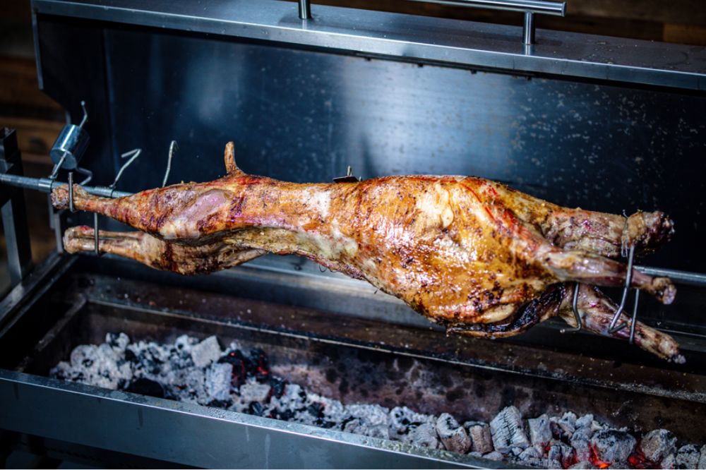 Whole lamb roasting on a spit rotisserie over hot charcoal.