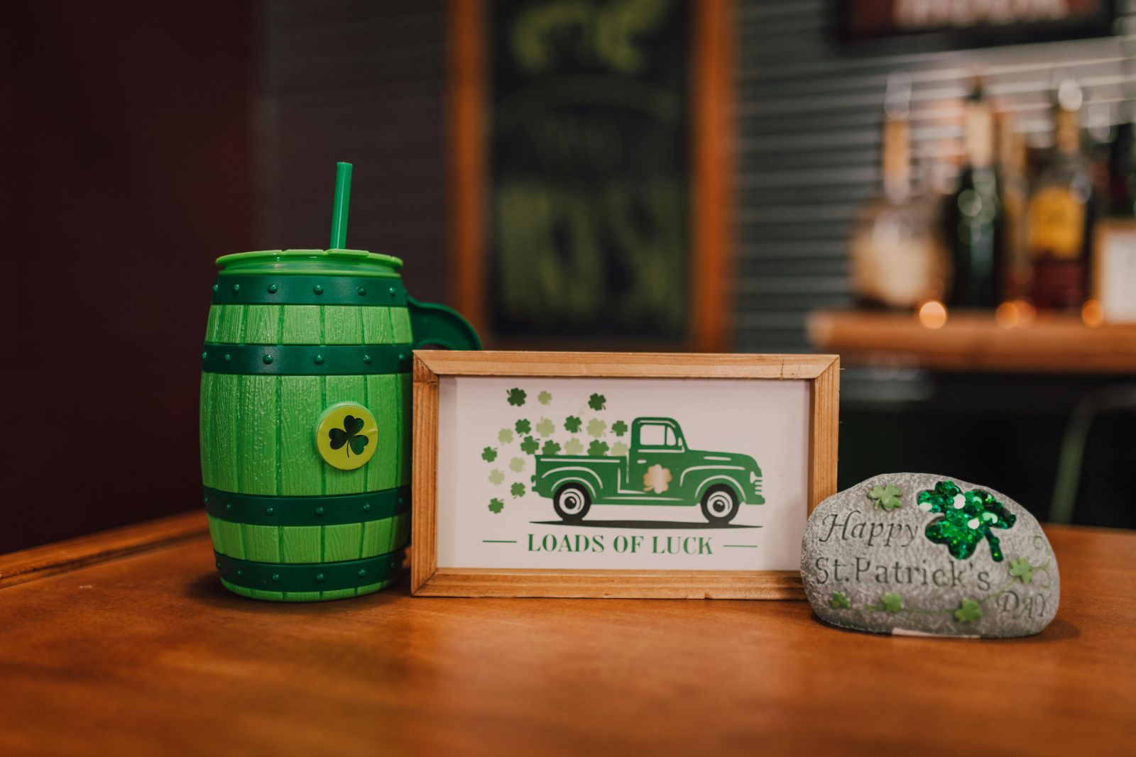 St Patrick’s Day display with green barrel mug, Loads of Luck sign and shamrock stone on wooden table