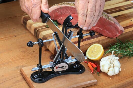 This is an image showing the Warthog classic II Knife Sharpener, Sharpening a knife with meat in the back ground