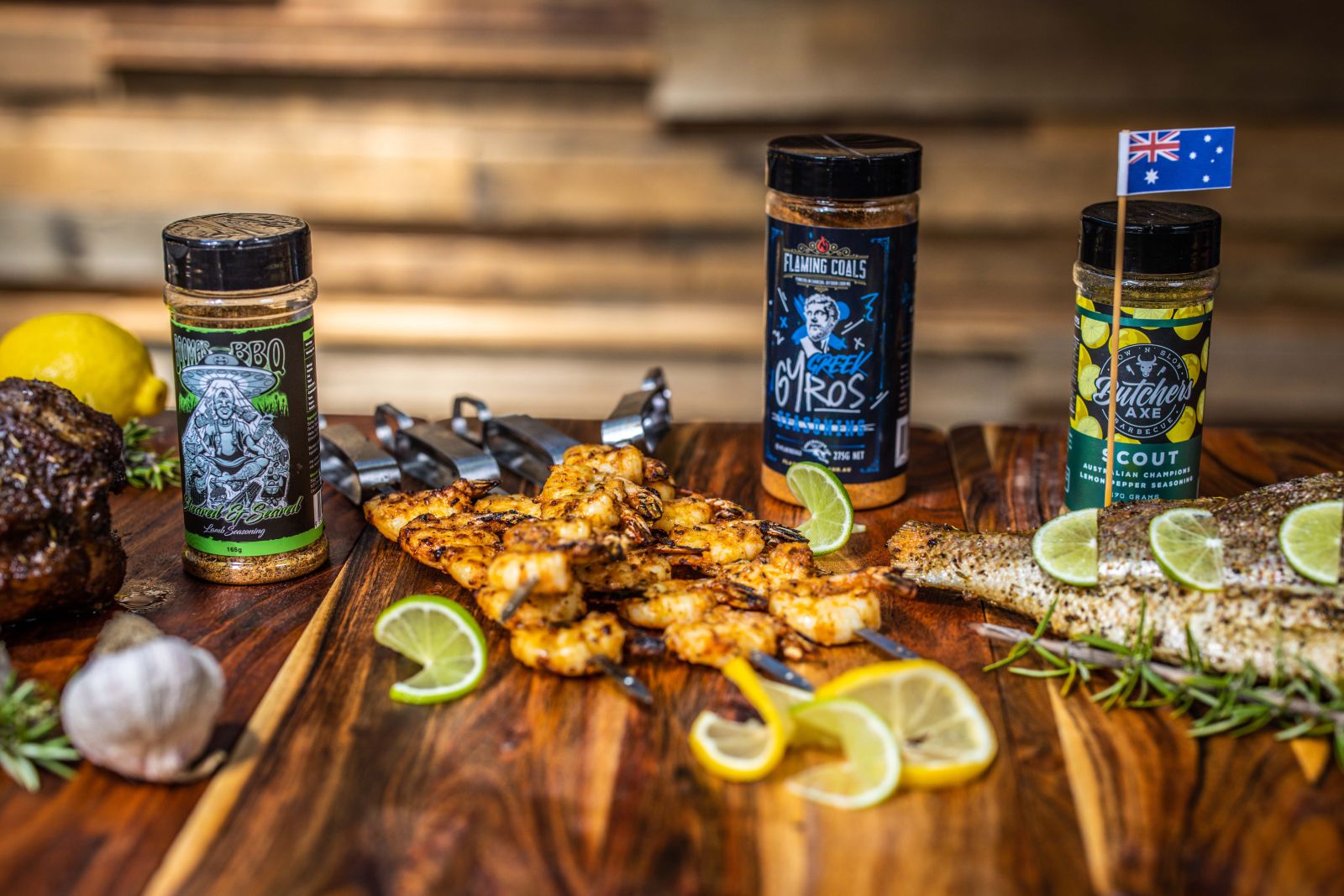 Seasoned prawns cooked on Auspit skewers, displayed on a wooden board alongside lemon slices, herbs, and Flaming Coals and Butchers Axe BBQ rubs
