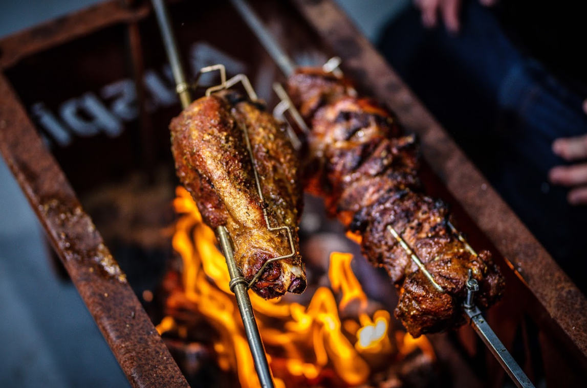 Lamb roasting on an Auspit over open flames during a campfire cook