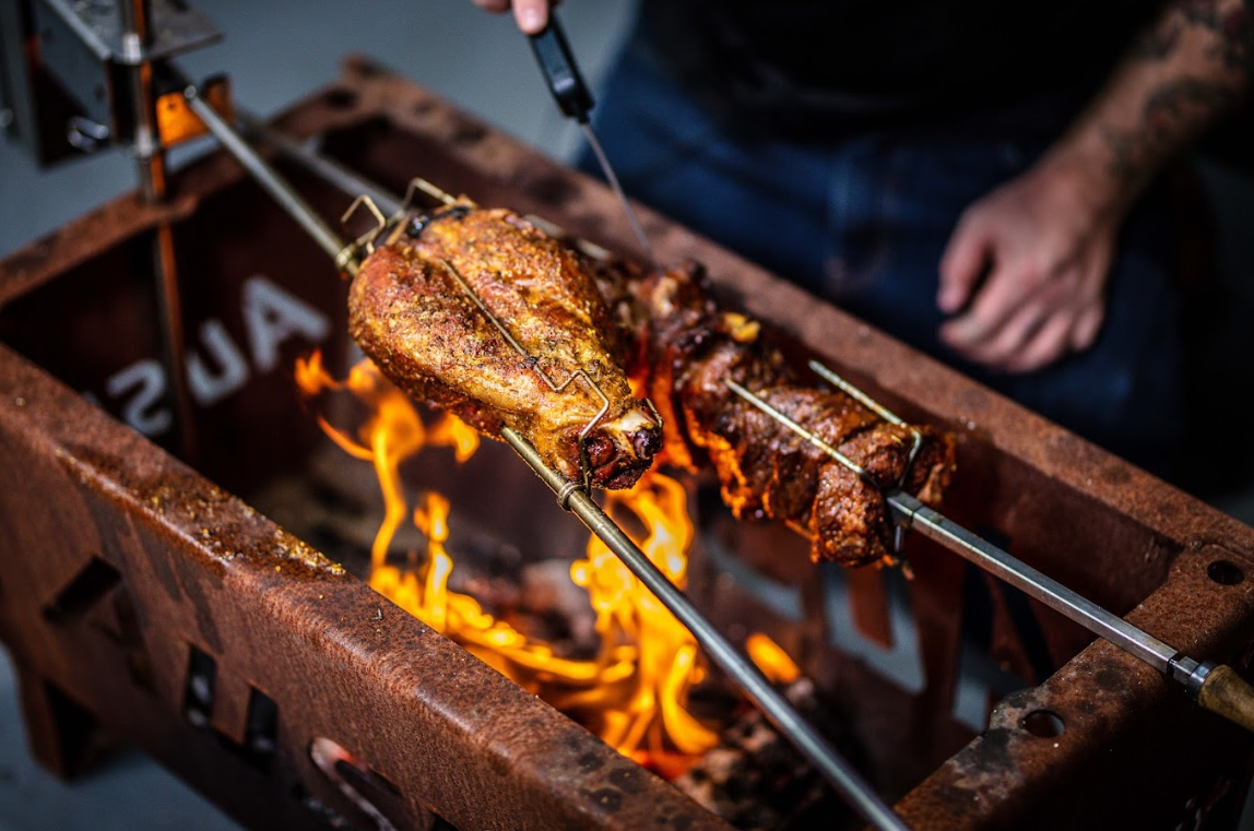 Checking the internal temperature of lamb roasting on a spit over open flames.