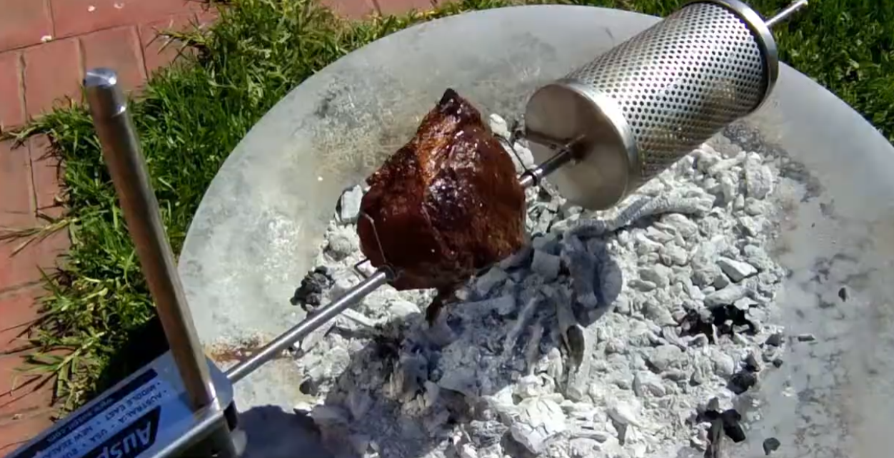 Beef roast cooking on an Auspit rotisserie over hot charcoal embers.
