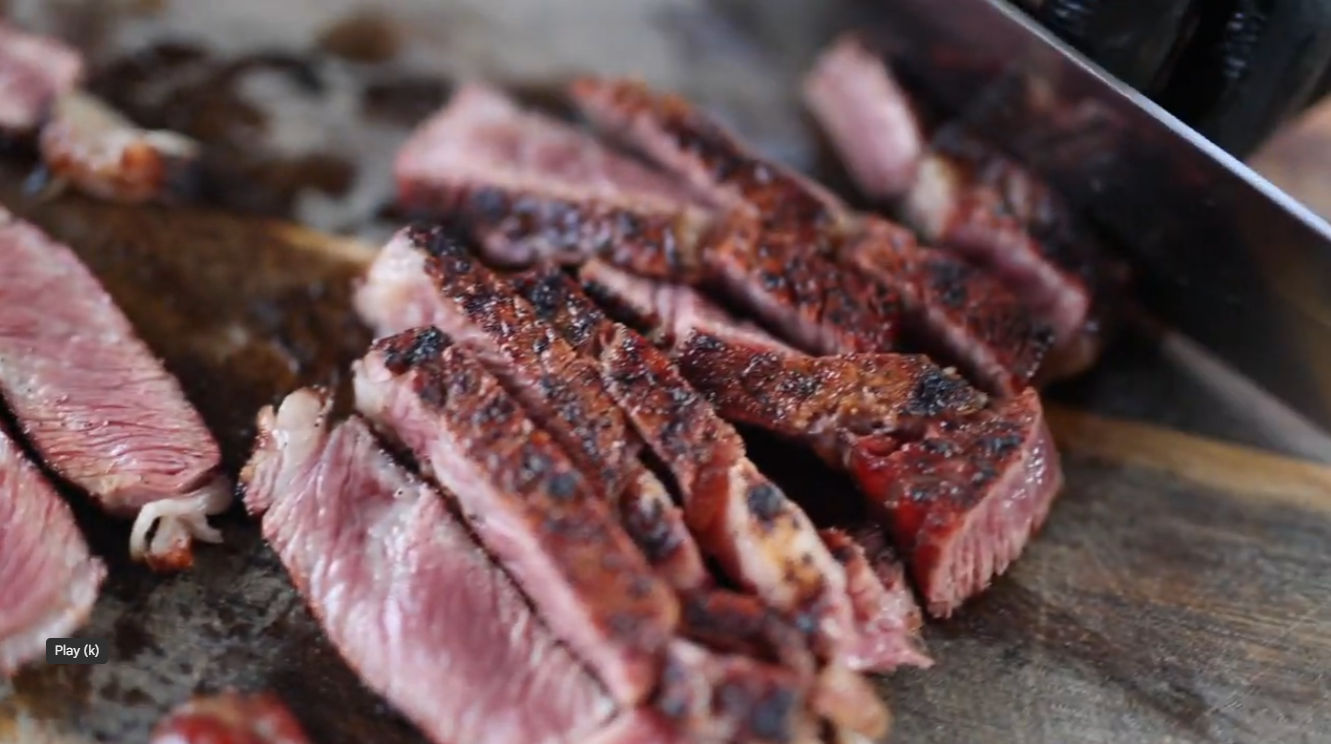 Sliced scotch fillet roast with a charred crust and juicy pink centre on a wooden cutting board.