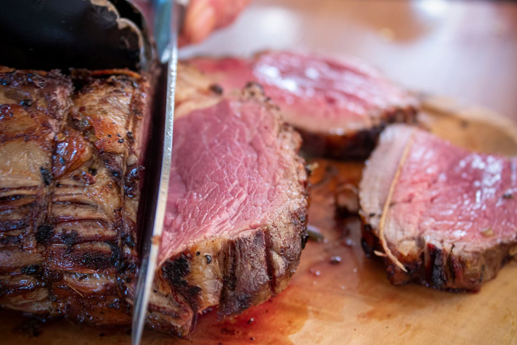 Slicing a charcoal roasted rump roast showing a juicy medium-rare centre on a wooden cutting board.