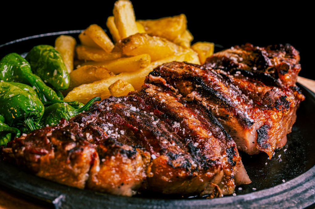 Charcoal roasted sirloin beef slices served with crispy chips and greens on a plate.