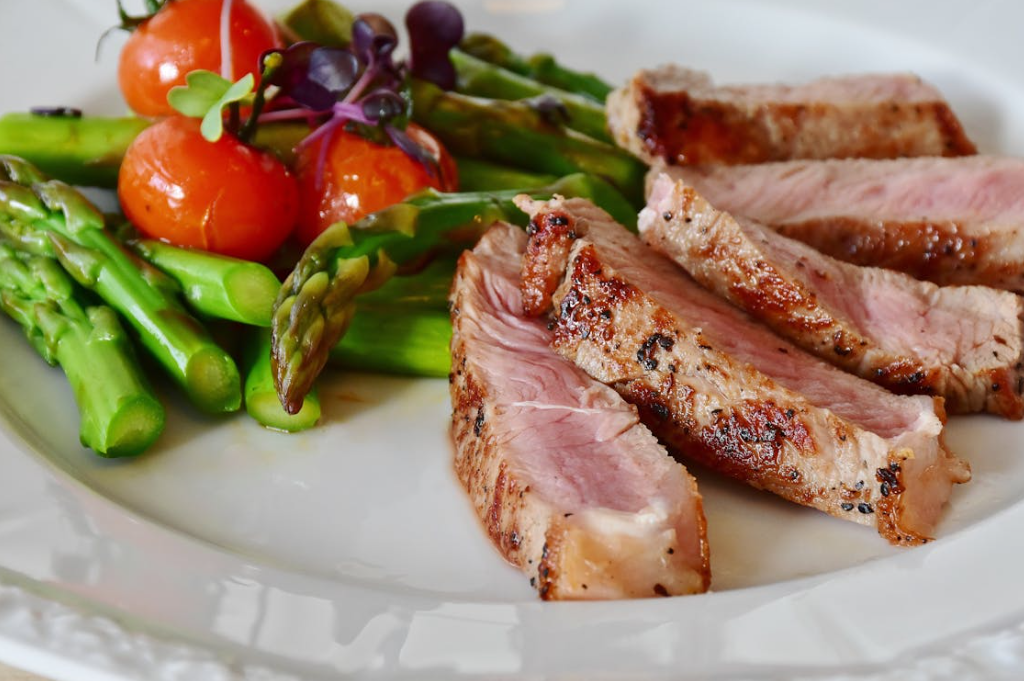 Sliced topside and silverside beef served with asparagus and roasted cherry tomatoes on a white plate.