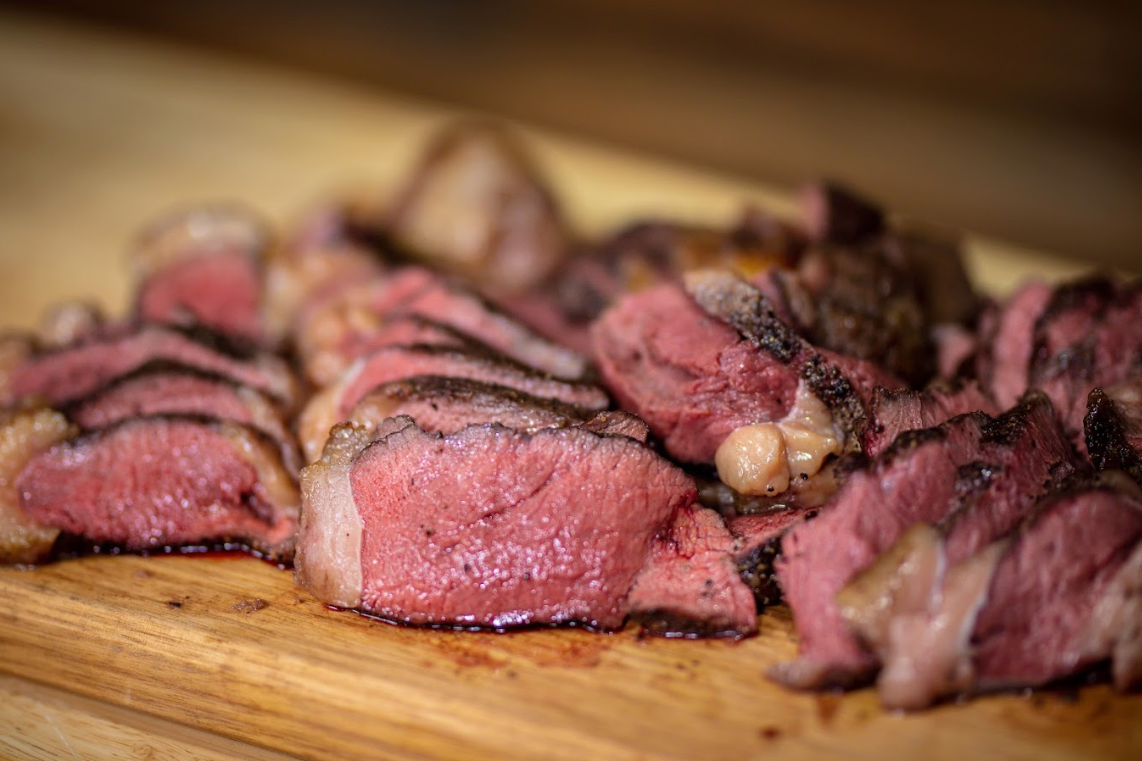 Sliced charcoal roasted picanha steak with a juicy pink centre and crispy fat cap on a wooden board.