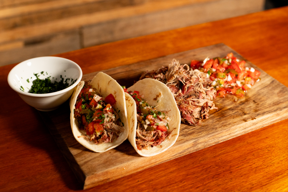 Pulled pork tacos served with fresh salsa and herbs on a wooden board.