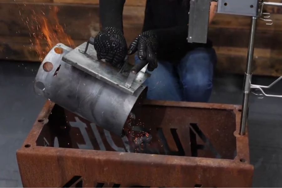 Charcoal being poured from a chimney starter into an Auspit fire pit to light the fire for cooking.