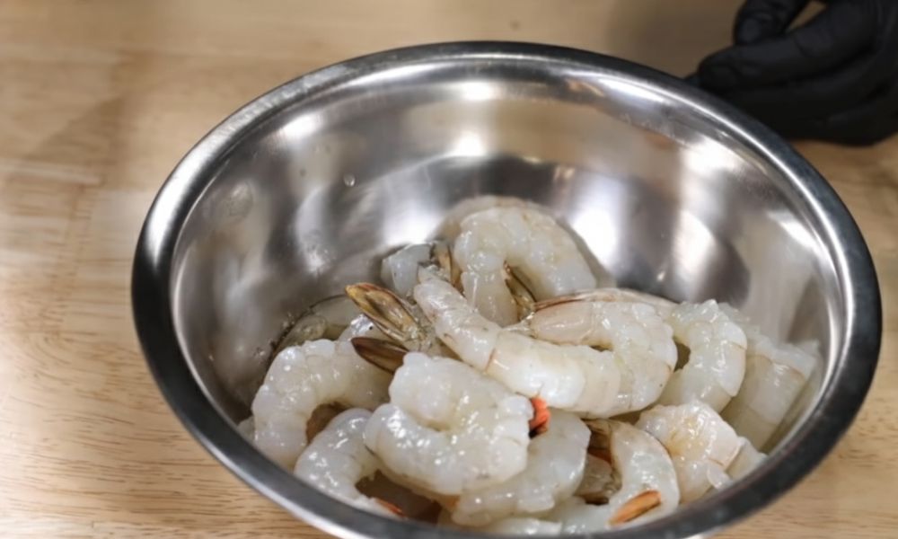 Fresh peeled prawns in a stainless steel mixing bowl, ready for seasoning and cooking.