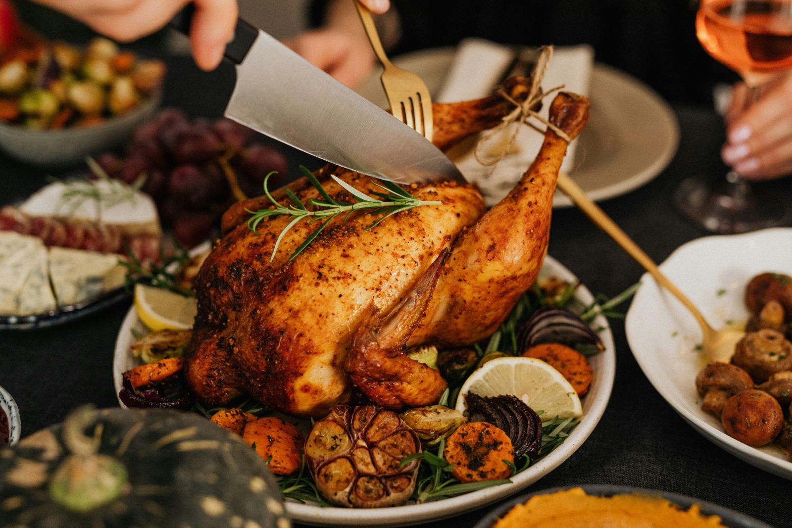 Carving a golden roasted chicken surrounded by herbs, lemon, and vegetables on a festive dinner table.