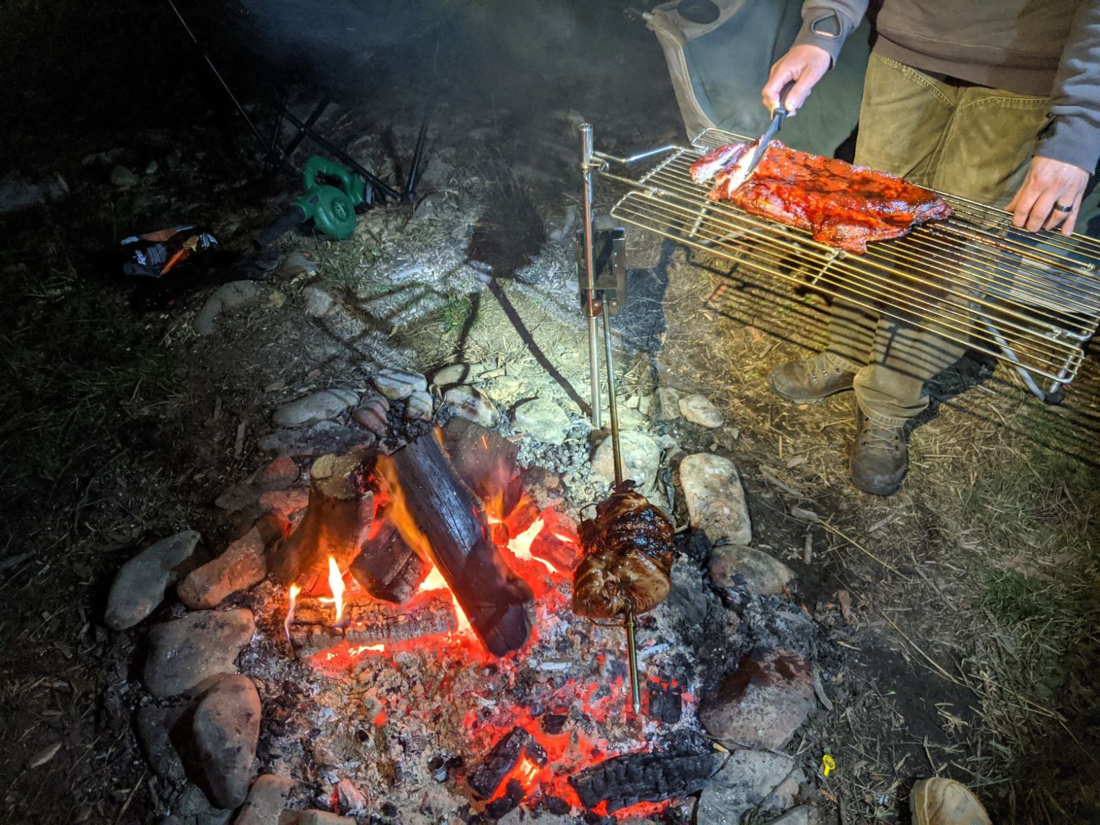 This image show the stainless steel folding camp grill being used as a carving tray. you can also see in the photo a spit roast cooking over a campfire