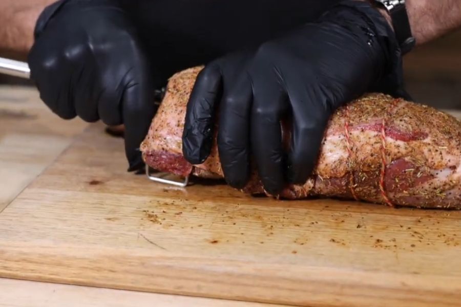 Seasoned and tied deboned leg of lamb being secured onto an Auspit skewer using squeeze lock spikes.